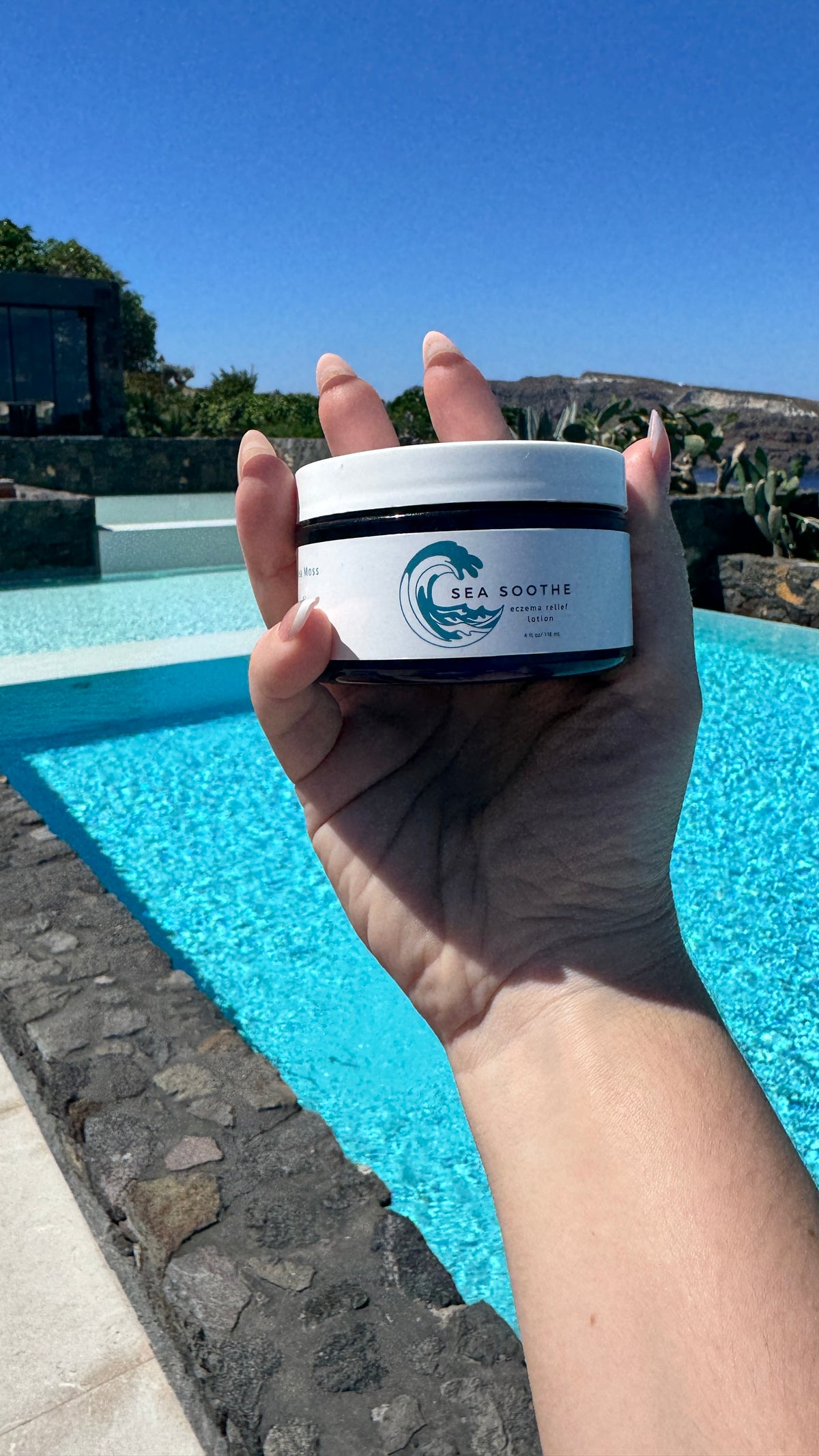 Hand holding a jar of Sea Soothe over blue water
